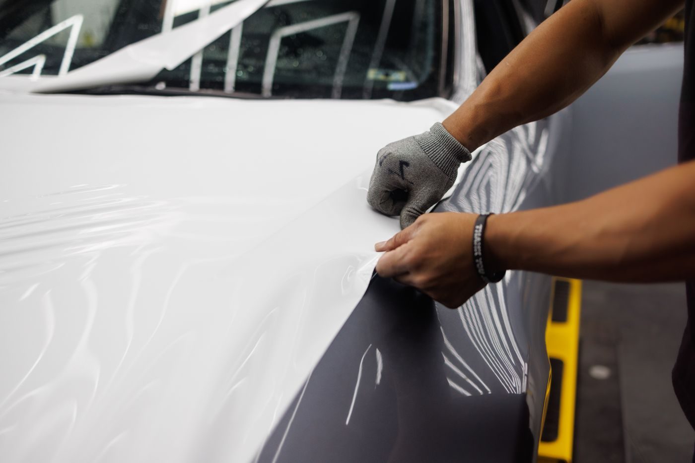Mains appliquant un film vinyle sur le capot d'une voiture